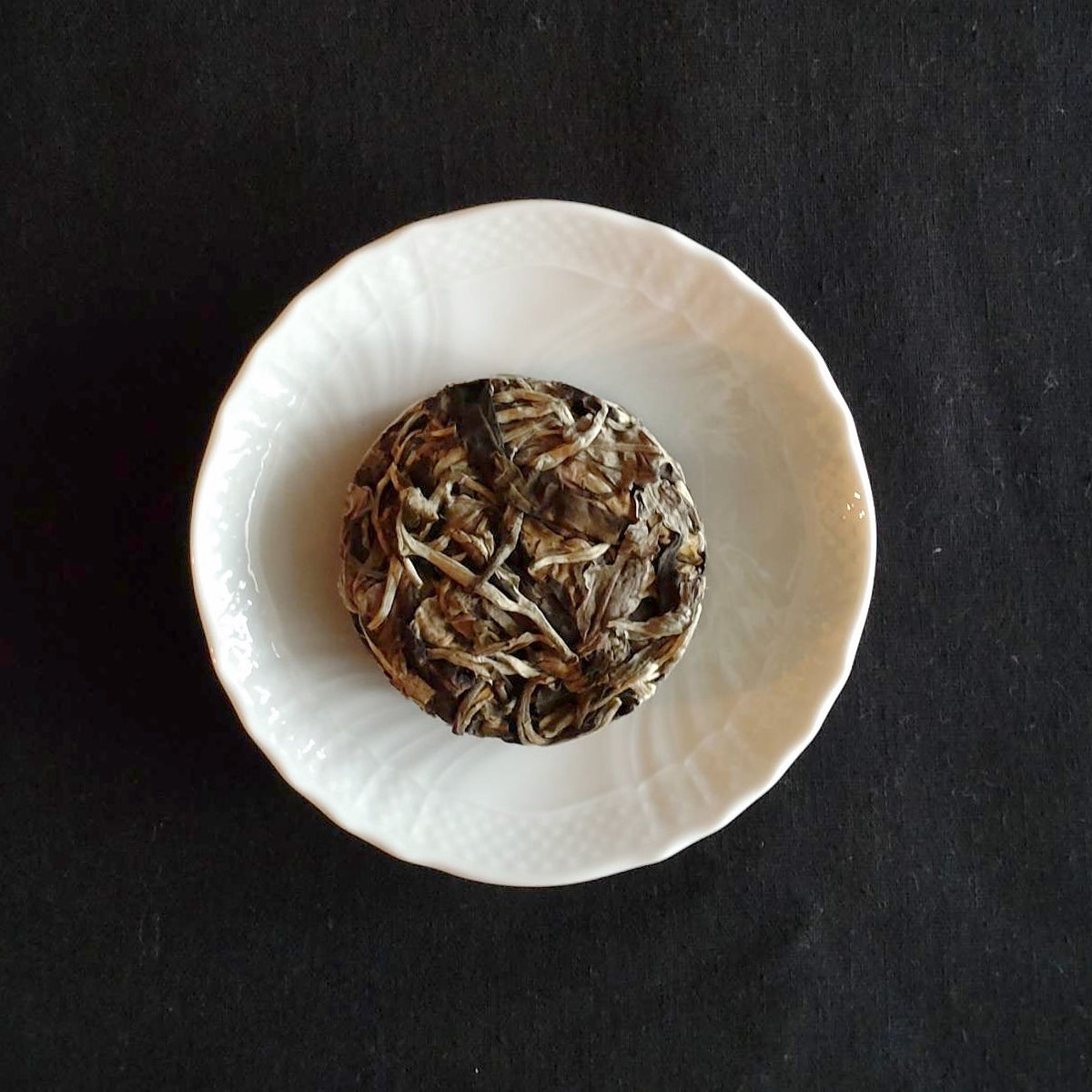月餅茶の茶餅。白磁の小皿に載った、満月のような円形の固形白茶